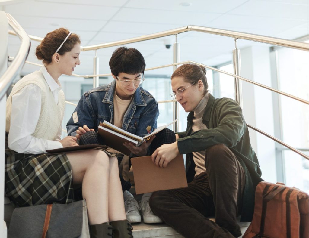 Group of university friends having a conversation while holding books on campus.