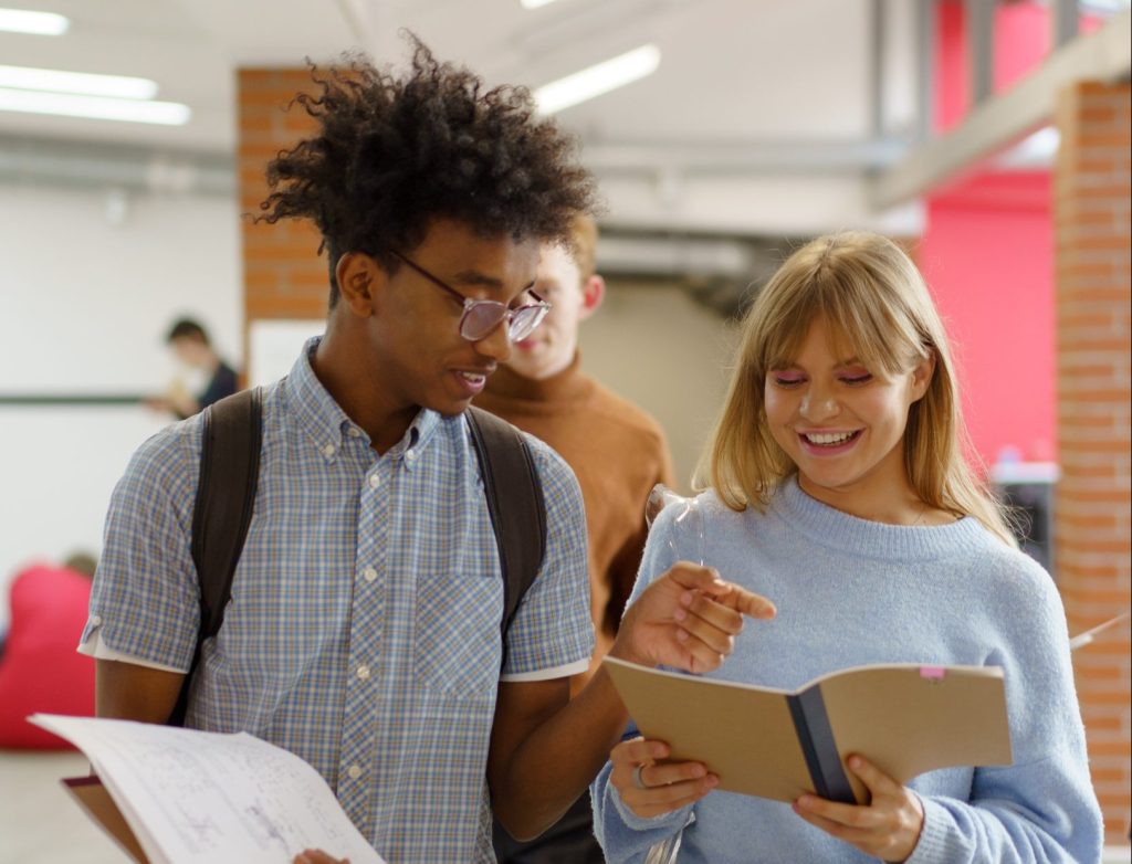 Young woman and man walking on campus, deep in discussion with books in hand.