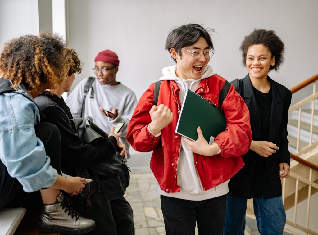 Group of university friends, books in hand, sharing happiness after class in a classroom.